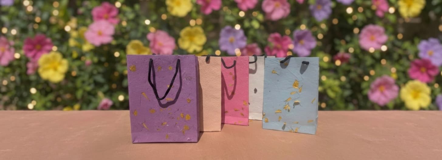 Seed Paper & Petal Bags — colorful plantable bags in purple, peach, pink and blue, flower garden background by Boxit